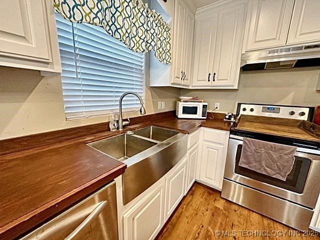 kitchen featuring under cabinet range hood, a sink, white cabinets, appliances with stainless steel finishes, and dark countertops