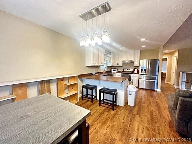 kitchen with appliances with stainless steel finishes, white cabinetry, a peninsula, wood finished floors, and under cabinet range hood