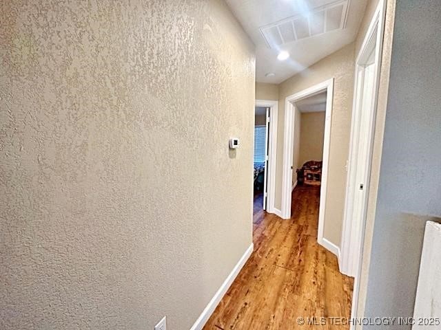 hallway with baseboards, a textured wall, and light wood-style floors