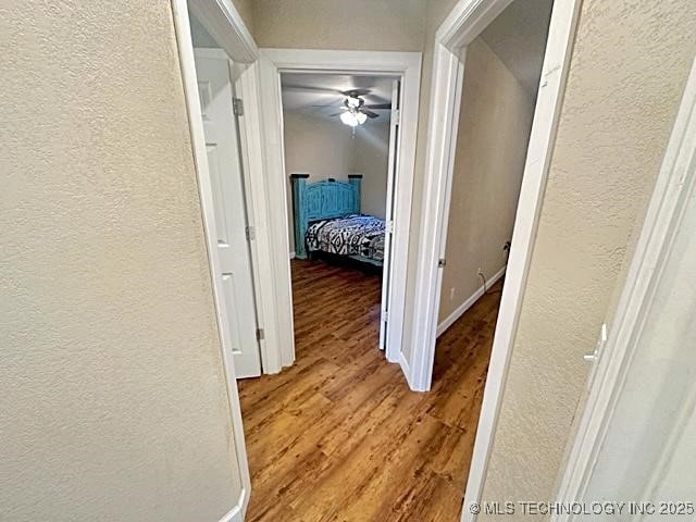 hall featuring baseboards, a textured wall, and light wood finished floors