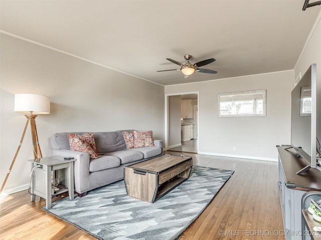 living room featuring ceiling fan, crown molding, baseboards, and wood finished floors