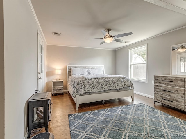 bedroom featuring crown molding, visible vents, ceiling fan, wood finished floors, and baseboards