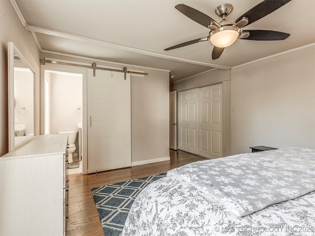 bedroom with a barn door, ensuite bath, wood finished floors, crown molding, and a closet