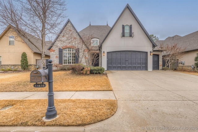 french country style house with a garage, concrete driveway, stone siding, and stucco siding