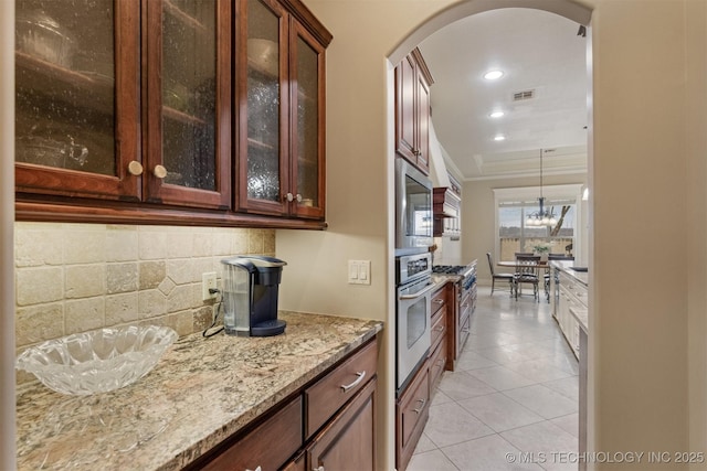 11870 S Oswego Ave, Tulsa, OK 74137 - kitchen featuring stainless steel appliances, arched walkways, tasteful backsplash, light stone countertops, and glass insert cabinets