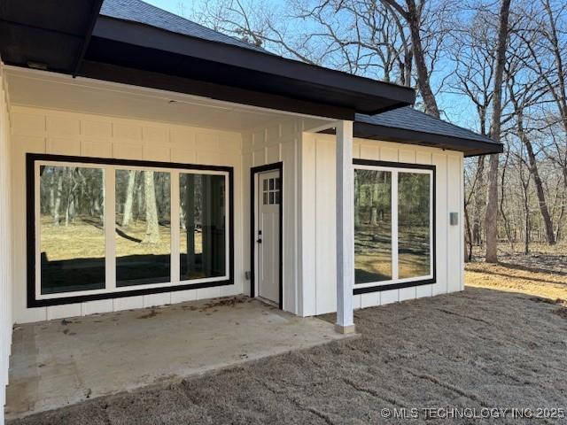 entrance to property with a patio, board and batten siding, and roof with shingles