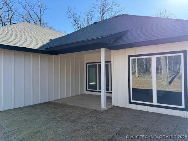 rear view of property with board and batten siding, roof with shingles, and a patio