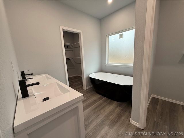 full bath with a freestanding tub, a spacious closet, a sink, and wood finished floors