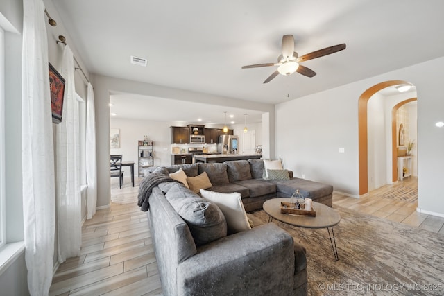 living area with visible vents, arched walkways, a ceiling fan, and wood finish floors