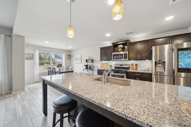 kitchen featuring light stone counters, stainless steel appliances, visible vents, backsplash, and a sink