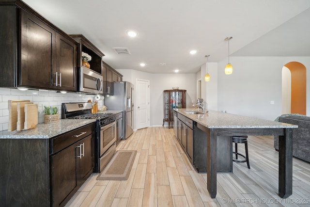 kitchen with dark brown cabinetry, tasteful backsplash, arched walkways, appliances with stainless steel finishes, and a kitchen breakfast bar