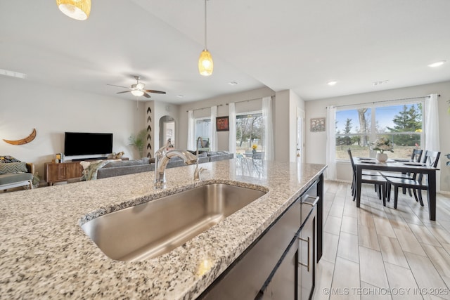 kitchen featuring arched walkways, light stone counters, a sink, open floor plan, and pendant lighting