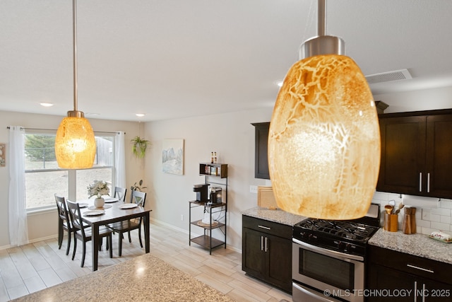 kitchen with light stone counters, dark brown cabinetry, visible vents, backsplash, and stainless steel gas stove