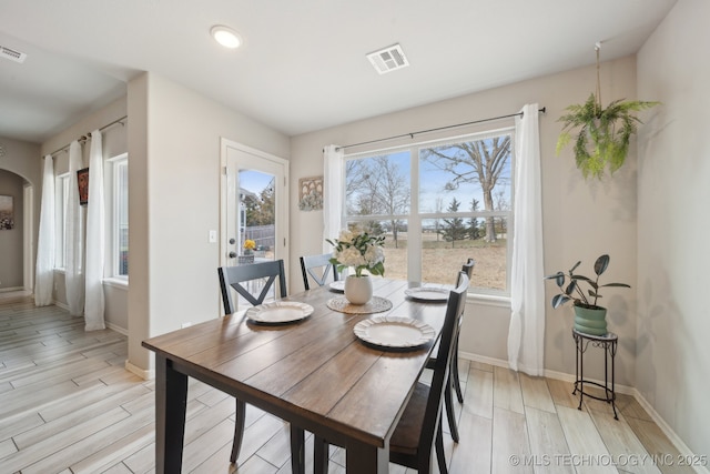 dining space featuring baseboards, visible vents, arched walkways, and wood finish floors