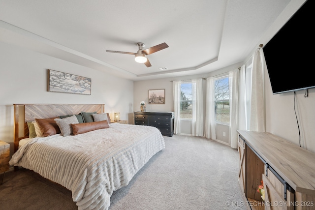 bedroom with a ceiling fan, a tray ceiling, light colored carpet, and visible vents