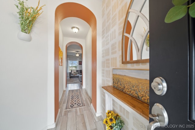 corridor featuring wood tiled floor, arched walkways, and baseboards