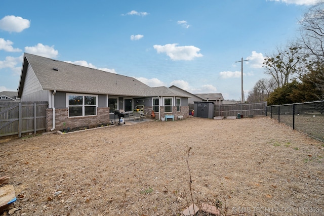 back of property with a shingled roof, a patio area, brick siding, and a fenced backyard