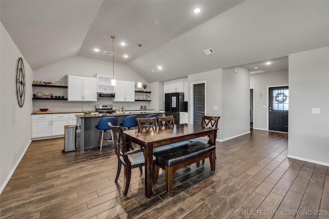 dining space featuring wood tiled floor, visible vents, vaulted ceiling, and baseboards