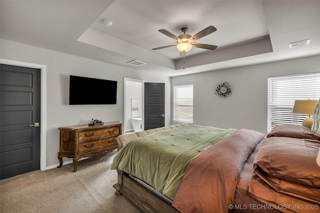 bedroom featuring light colored carpet, a raised ceiling, visible vents, and connected bathroom