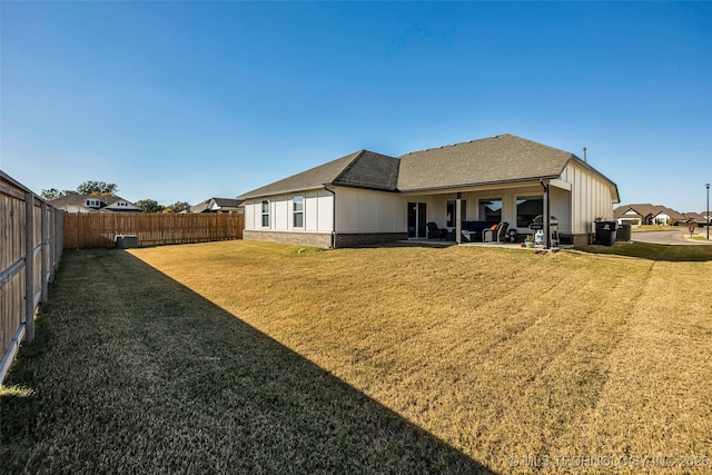 rear view of house with roof with shingles, a yard, brick siding, a patio, and a fenced backyard