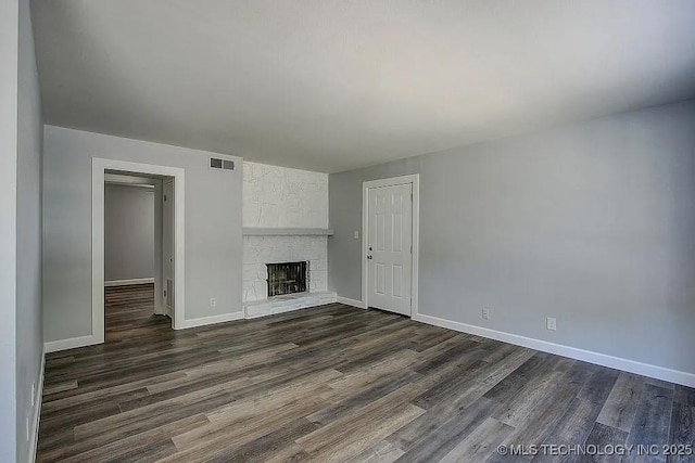 unfurnished living room with a stone fireplace, dark wood-style flooring, visible vents, and baseboards