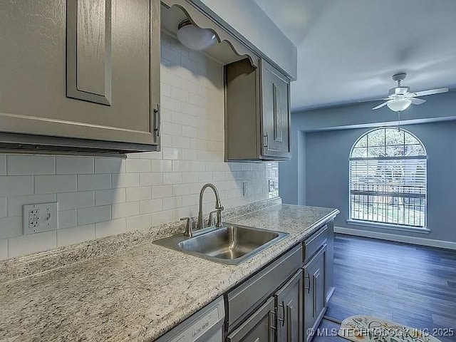 kitchen featuring dark wood finished floors, decorative backsplash, a sink, ceiling fan, and baseboards