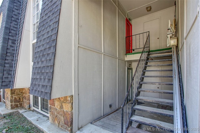 doorway to property with stone siding and a shingled roof