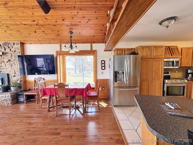 kitchen featuring stainless steel appliances, dark countertops, brown cabinetry, and light wood finished floors