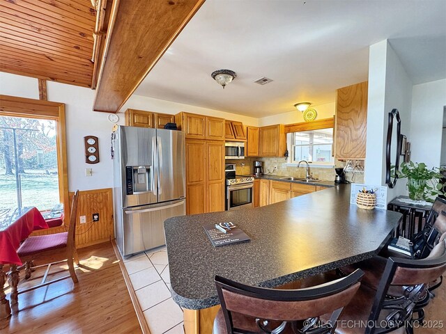 32432 S Skyline Dr, Cookson, OK 74427 - kitchen featuring appliances with stainless steel finishes, a peninsula, dark countertops, a breakfast bar area, and wainscoting