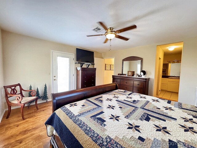 bedroom with light wood-style floors, ensuite bath, visible vents, and a ceiling fan