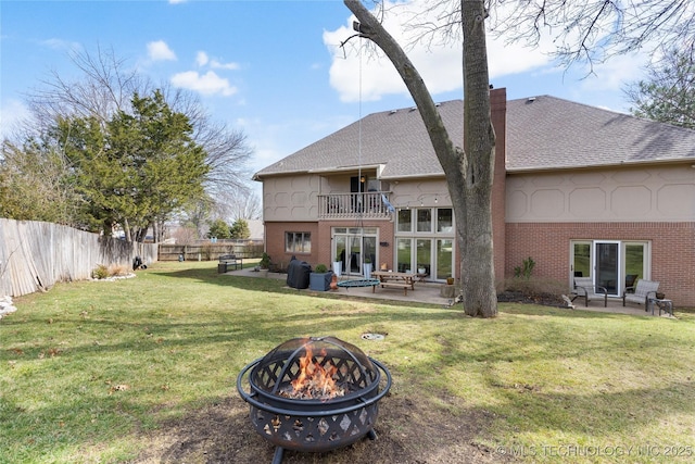 rear view of property featuring a fire pit, a patio, a balcony, a fenced backyard, and brick siding