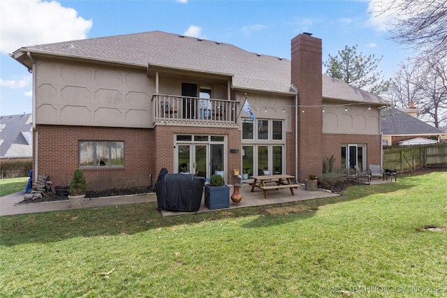 rear view of property with a balcony, brick siding, fence, a lawn, and a chimney