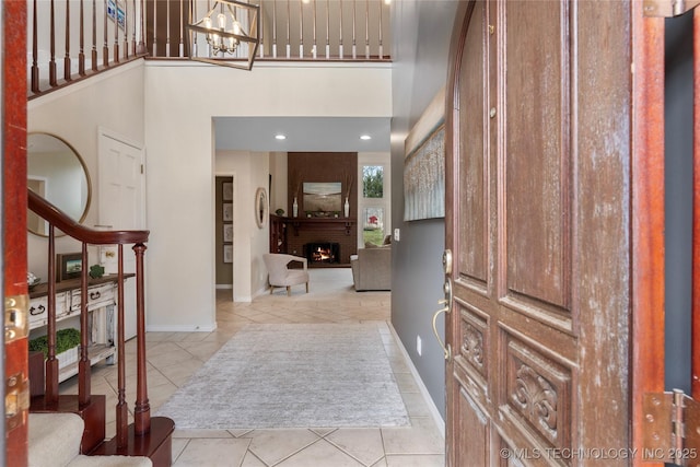 entryway with baseboards, a towering ceiling, stairs, a fireplace, and a notable chandelier