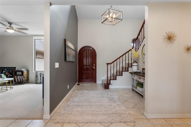 tiled entryway featuring arched walkways, stairway, carpet flooring, baseboards, and ceiling fan with notable chandelier