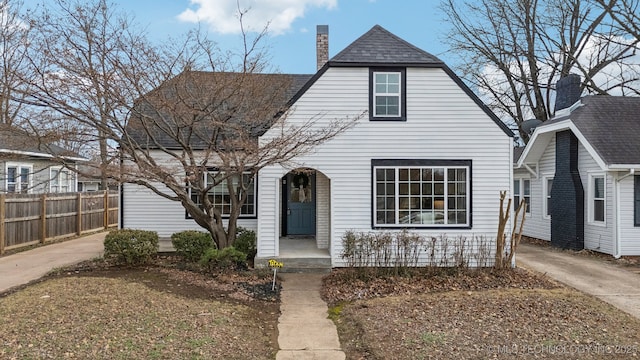 view of front facade with driveway, a shingled roof, a chimney, and fence