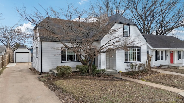 view of front of property with an outbuilding, a detached garage, a chimney, concrete driveway, and fence