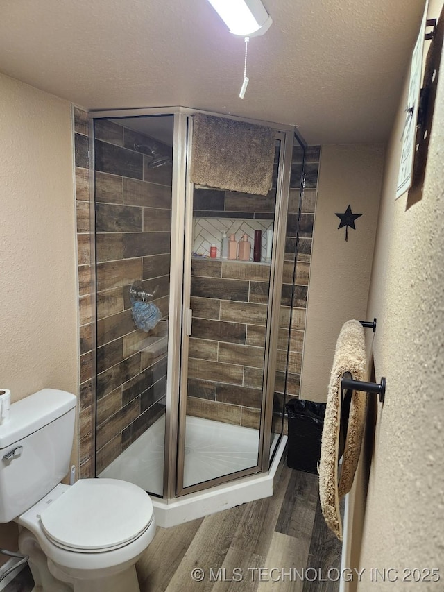 bathroom featuring a textured wall, toilet, wood finished floors, a textured ceiling, and a shower stall