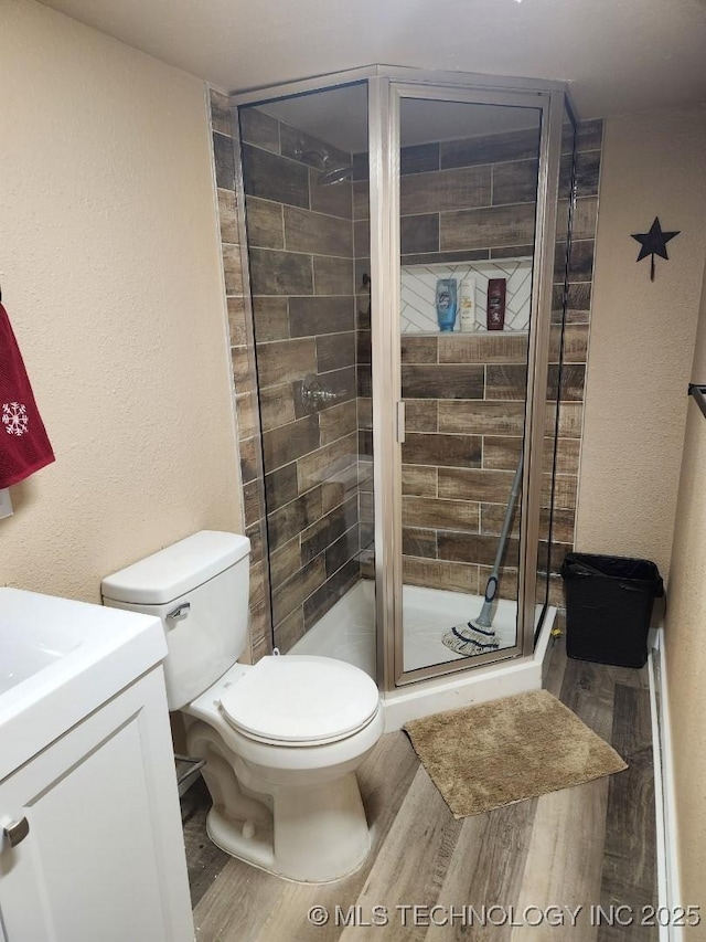 bathroom with a textured wall, toilet, wood finished floors, vanity, and a shower stall