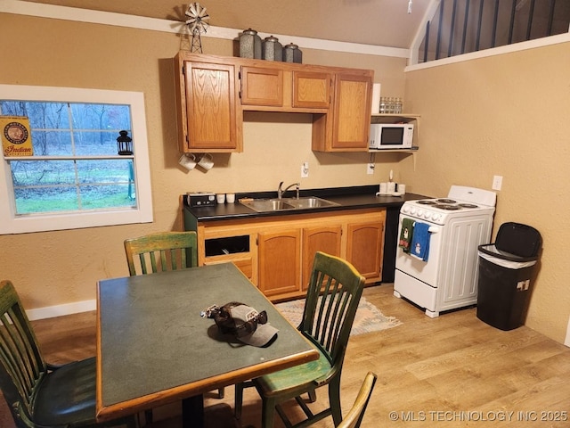 kitchen with dark countertops, white appliances, a sink, and light wood finished floors