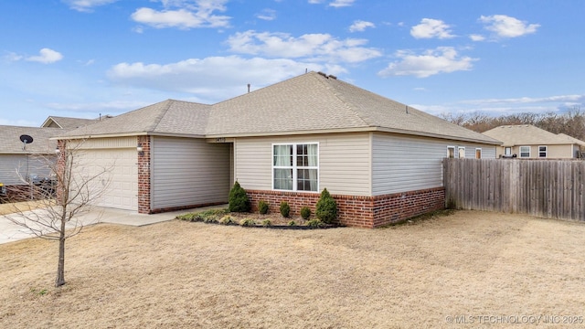 view of side of property featuring brick siding, roof with shingles, an attached garage, and fence