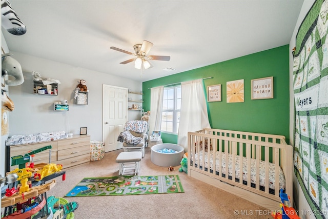 carpeted bedroom with a nursery area and a ceiling fan