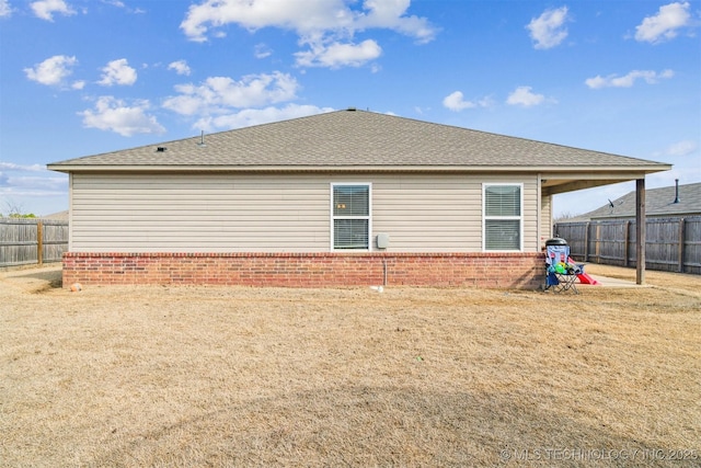 back of property with a shingled roof, brick siding, and fence