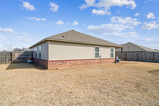 back of house featuring brick siding, roof with shingles, and a fenced backyard