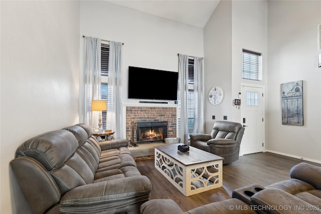 living area featuring a fireplace, a towering ceiling, baseboards, and wood finished floors