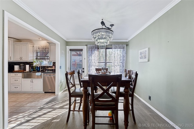 dining space with baseboards, ornamental molding, wood finished floors, and an inviting chandelier