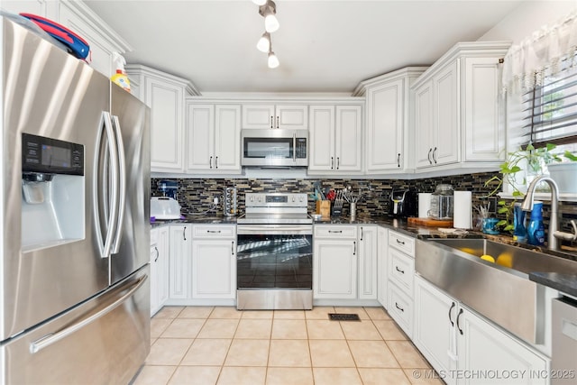 kitchen featuring light tile patterned floors, dark countertops, appliances with stainless steel finishes, a sink, and backsplash