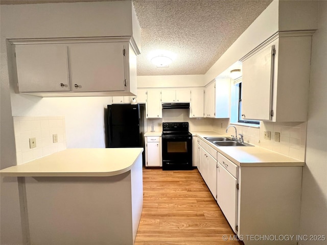 kitchen with light wood-style flooring, under cabinet range hood, a peninsula, a sink, and black appliances