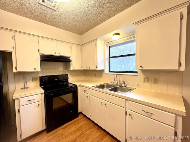 kitchen with light wood finished floors, visible vents, a sink, under cabinet range hood, and black appliances