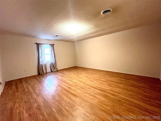 spare room with a textured ceiling, visible vents, and wood finished floors