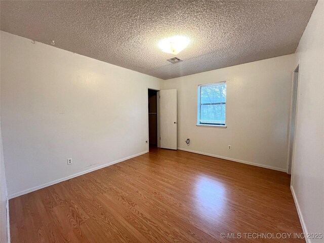 spare room featuring baseboards, a textured ceiling, visible vents, and wood finished floors